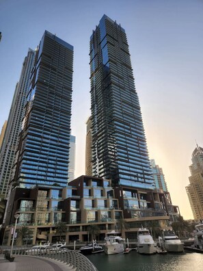 Two tall, modern skyscrapers with reflective glass facades, a marina with boats, and a waterfront promenade.