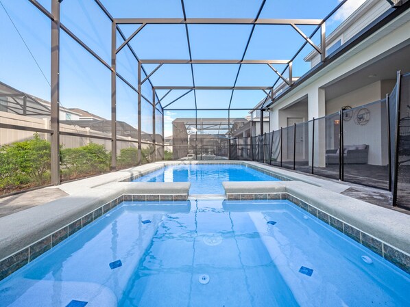 Une piscine dotée d’un toit en verre, entourée d’une clôture et d’un patio couvert.