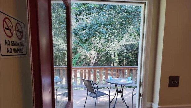 A door leading to an outdoor deck with a table and chairs, a no smoking and no vaping sign, and a view of trees. - Quiet retreat (Macon)