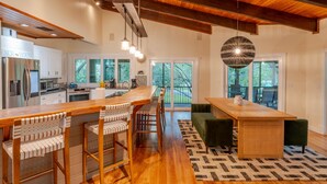 A spacious kitchen with wooden beams, a large island with bar stools, and a view of the outdoors through large windows. - 2 Home Sport Complex W/ Private Lake & Theater! (Jensen Beach)