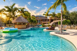 A resort pool area with a clear blue pool, lounge chairs, and a thatched hut. - 2 Home Sport Complex W/ Private Lake & Theater! (Jensen Beach)