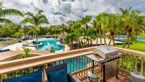 A poolside area with a barbecue grill, lounge chairs, and a view of a swimming pool surrounded by palm trees. - 2 Home Sport Complex W/ Private Lake & Theater! (Jensen Beach)