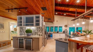 A modern kitchen with wooden ceiling beams, built-in cabinets, and a central island with a sink and a potted plant. - 2 Home Sport Complex W/ Private Lake & Theater! (Jensen Beach)