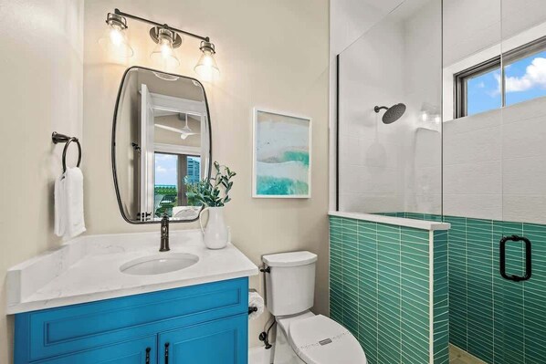 A bathroom with a white sink, blue vanity, a white toilet, and a shower area with green tiles.
