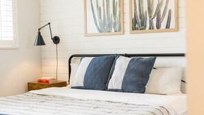 A neatly made bed with striped bedding, a bedside lamp, and two framed cactus paintings on the wall. - 10 Min to Downtown~Luxury Home w/ Pool, Outdoor TV (Austin)