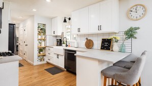 A modern kitchen with white cabinets, a black refrigerator, and a wooden countertop. - 10 Min to Downtown~Luxury Home w/ Pool, Outdoor TV (Austin)