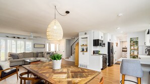 A modern kitchen with white cabinets, a wooden dining table, and a hanging light fixture. - 10 Min to Downtown~Luxury Home w/ Pool, Outdoor TV (Austin)
