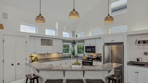 Cozinha moderna com armários brancos, bancadas de granito, uma ilha central com banquetas e iluminação pendente.