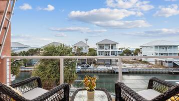 A balcony with wicker chairs and a table, overlooking a marina with boats and buildings.