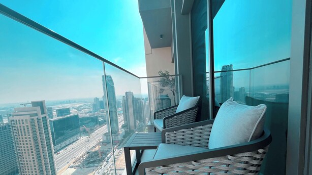 Un balcon situé dans un immeuble de grande hauteur, offrant une vue sur la ville, doté de mobilier moderne et d’une rambarde en verre.