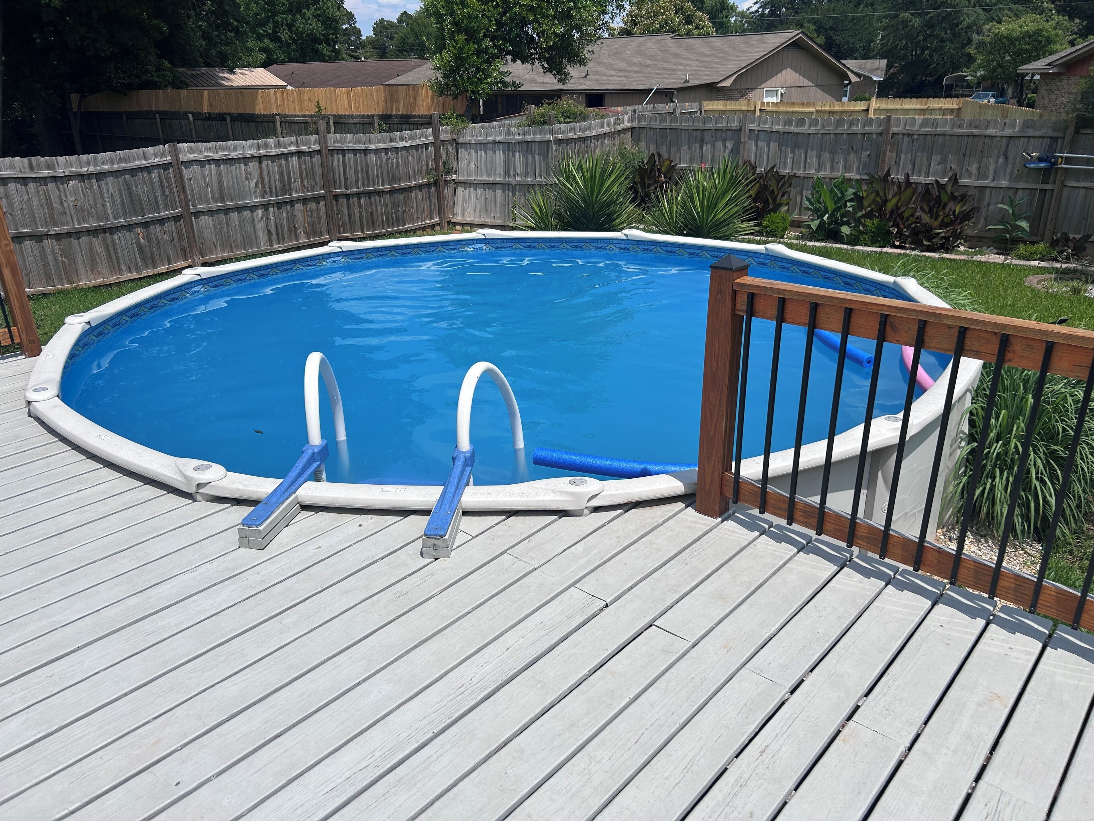 An outdoor swimming pool with a wooden deck and a wooden fence in the background.