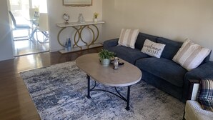 A living room with a dark blue sofa, a round coffee table, and a patterned rug. - Visiting family need space? Enjoy our spacious & serene abode. Plenty of space! (Warner Robins)