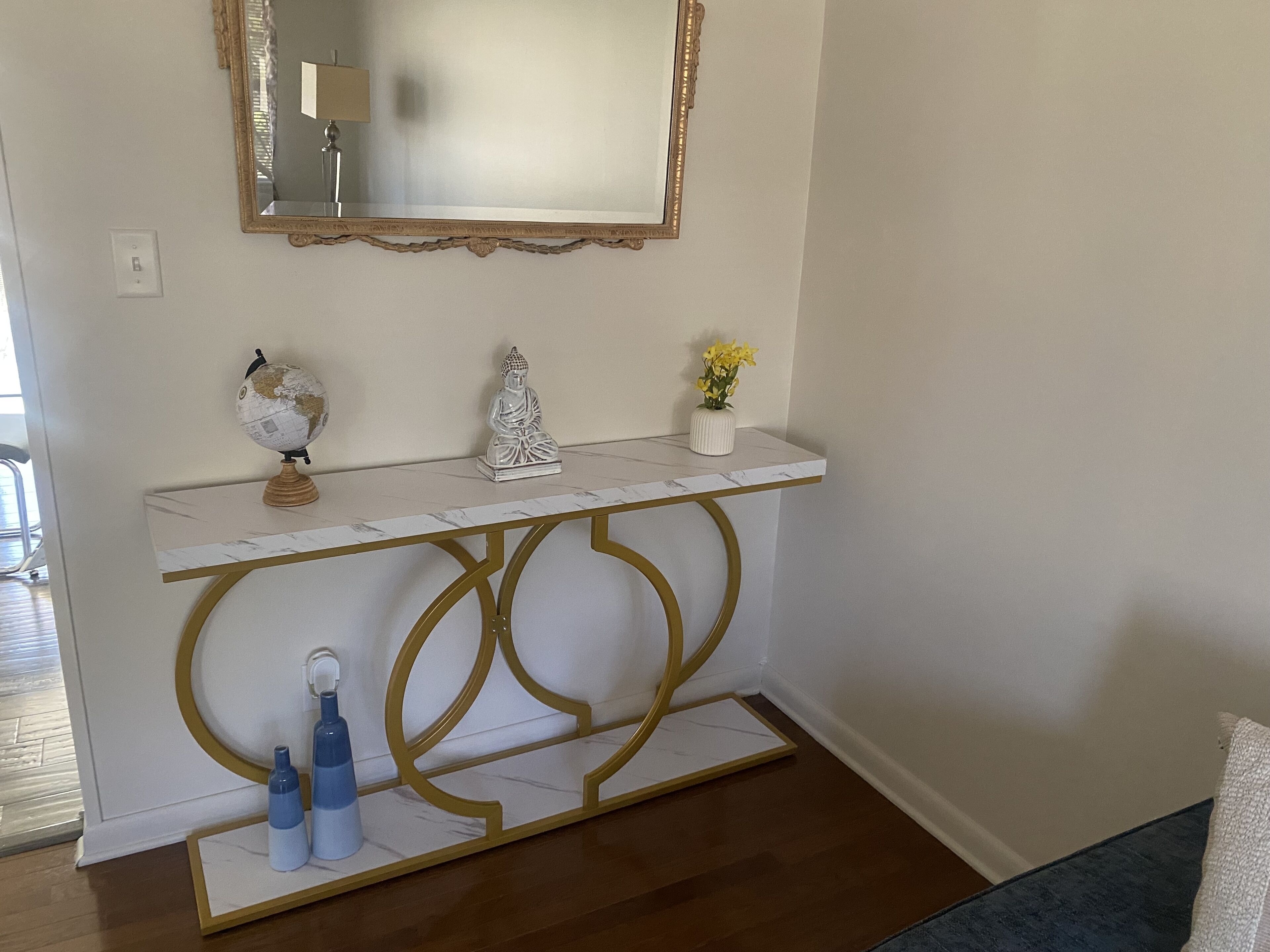 Una consolle bianca con dettagli dorati, un mappamondo, una statua di Buddha e un vaso con fiori gialli.