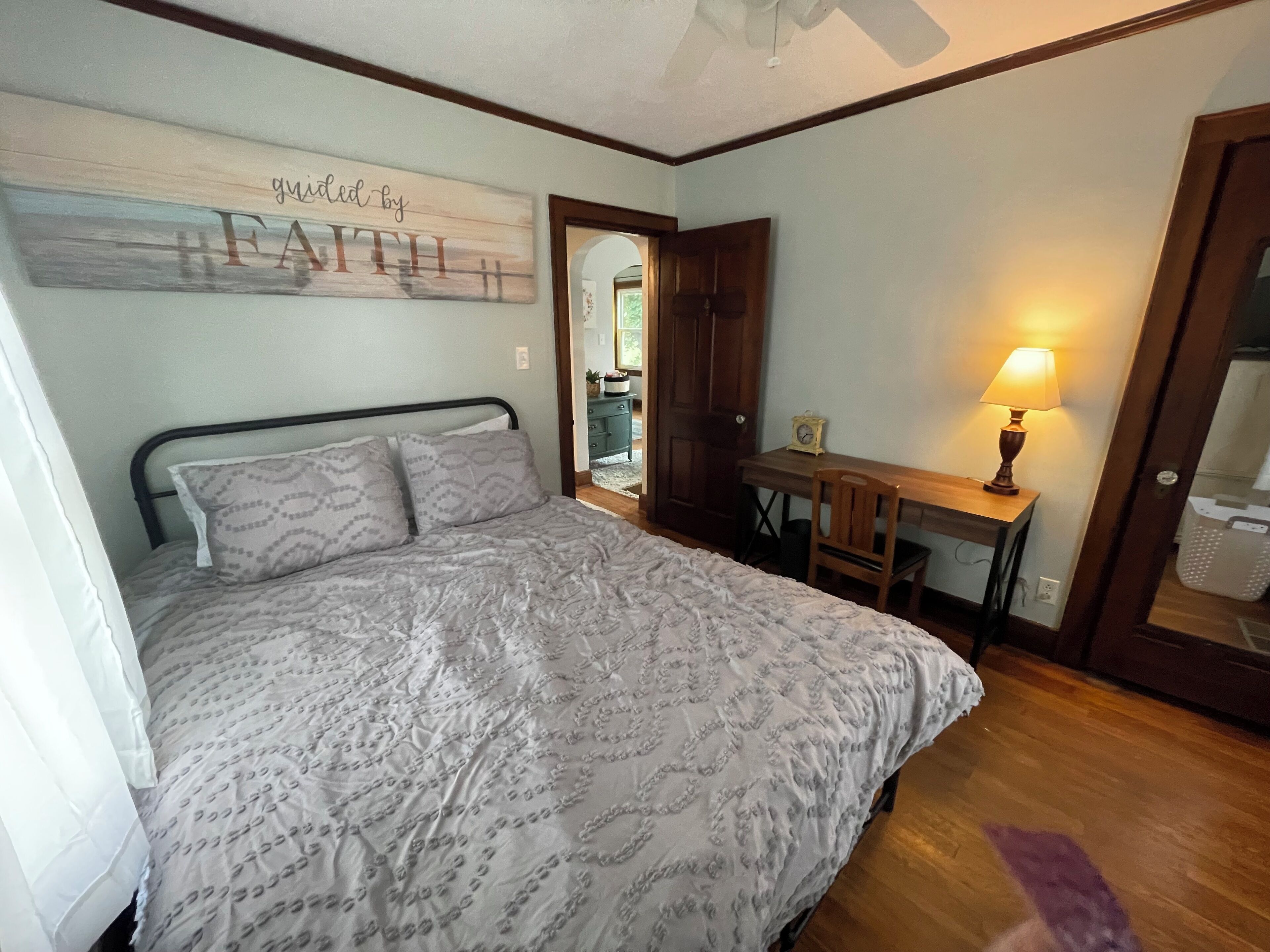 A bedroom with a bed, a desk, a chair, a lamp, and a wall sign.