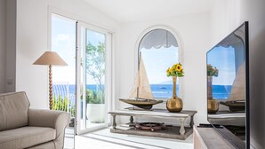 A living room with a sofa, a table with decorative items, a lamp, and a television. - Villa Biancalisa - Sea View Infinity Pool - Newly refurbished - Beachfront (Massa Lubrense)
