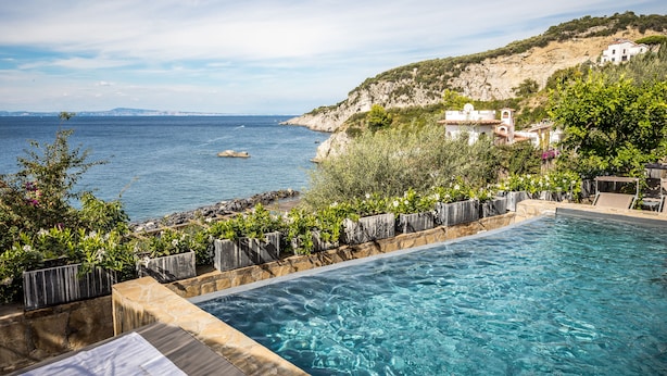 A swimming pool with a view of the sea and a hillside with buildings. - Villa Biancalisa - Sea View Infinity Pool - Newly refurbished - Beachfront (Massa Lubrense)