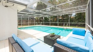 Zona de piscina exterior cubierta con sillas reclinables azules y una mesa pequeña con plantas.