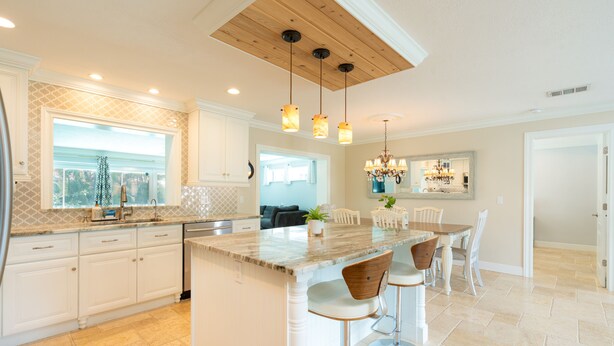 Una cocina moderna con una isla central, iluminación colgante y una zona de comedor con taburetes de bar.