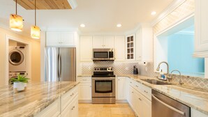 Una cocina moderna con armarios blancos, electrodomésticos de acero inoxidable, encimera de mármol e iluminación colgante.