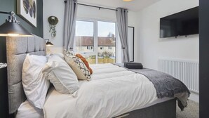 Een slaapkamer met een bed, een aan de muur bevestigde televisie, een raam met gordijnen en een radiator.