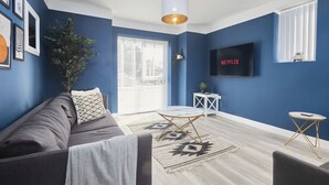 Een woonkamer met een blauwe wand, een grijze bank, een witte salontafel en een aan de muur bevestigde televisie.