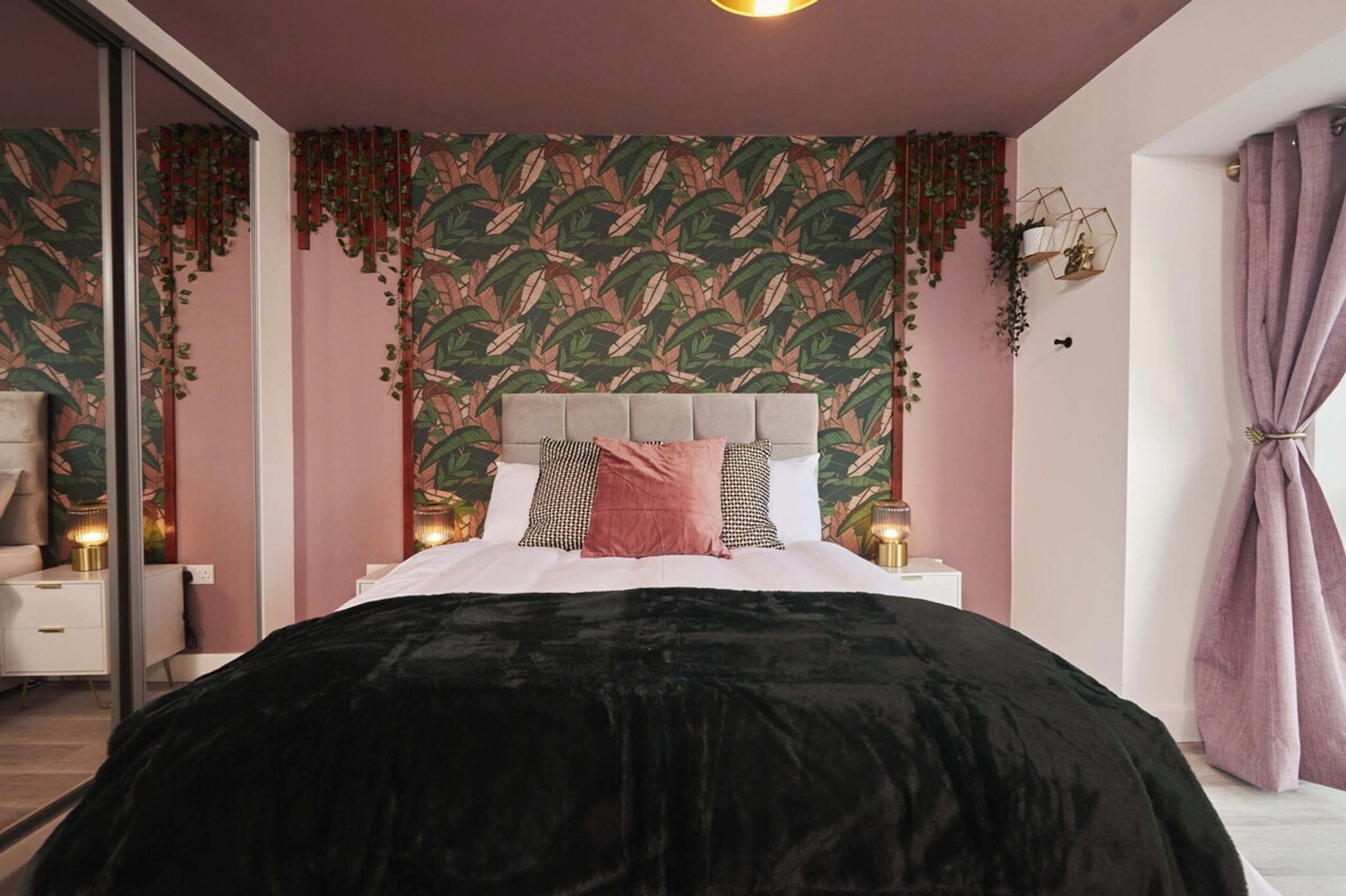 A bedroom with a bed, bedside tables, a mirror, and a window with curtains.