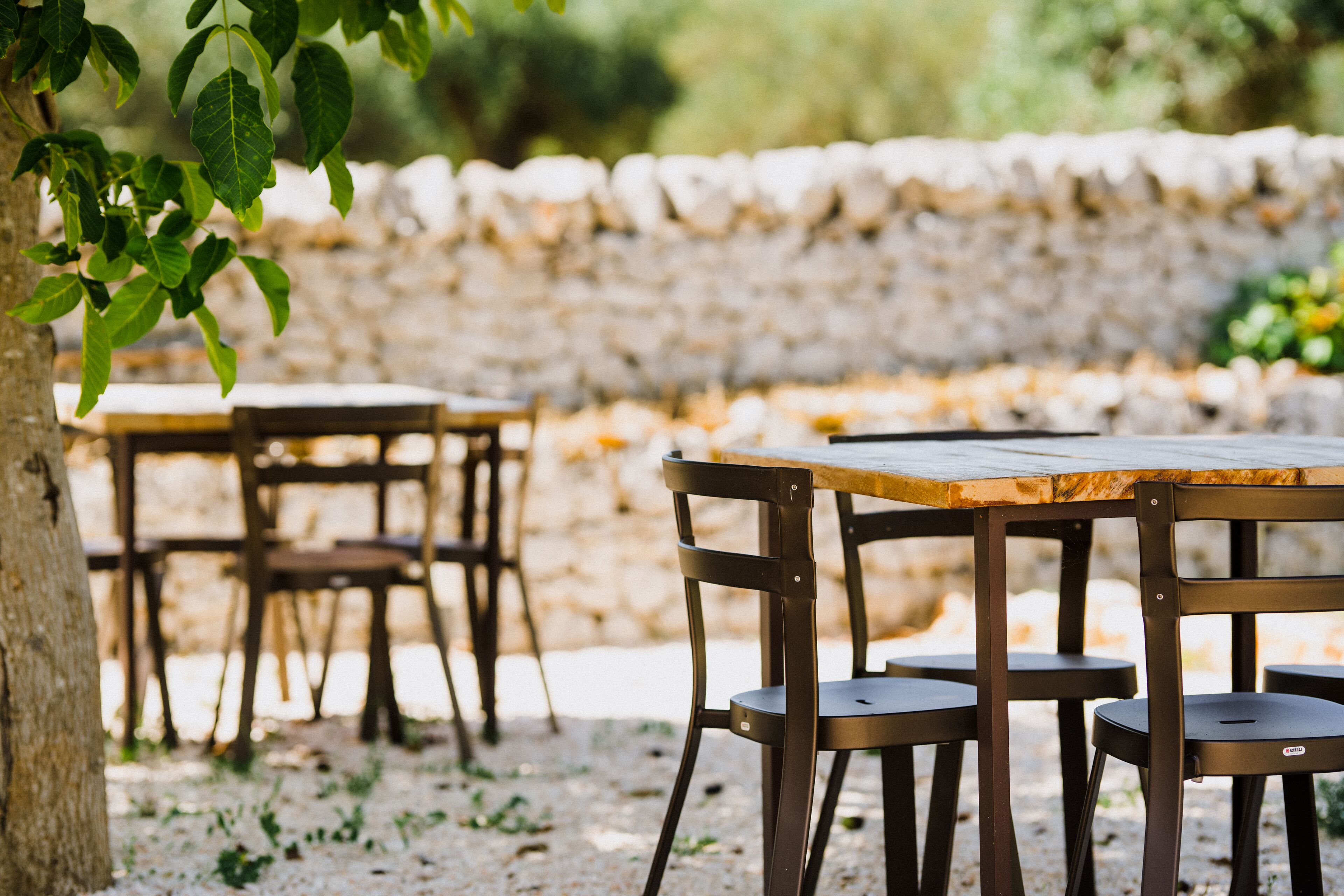 Zona pranzo all'aperto con pareti in pietra e tavoli e sedie in legno.
