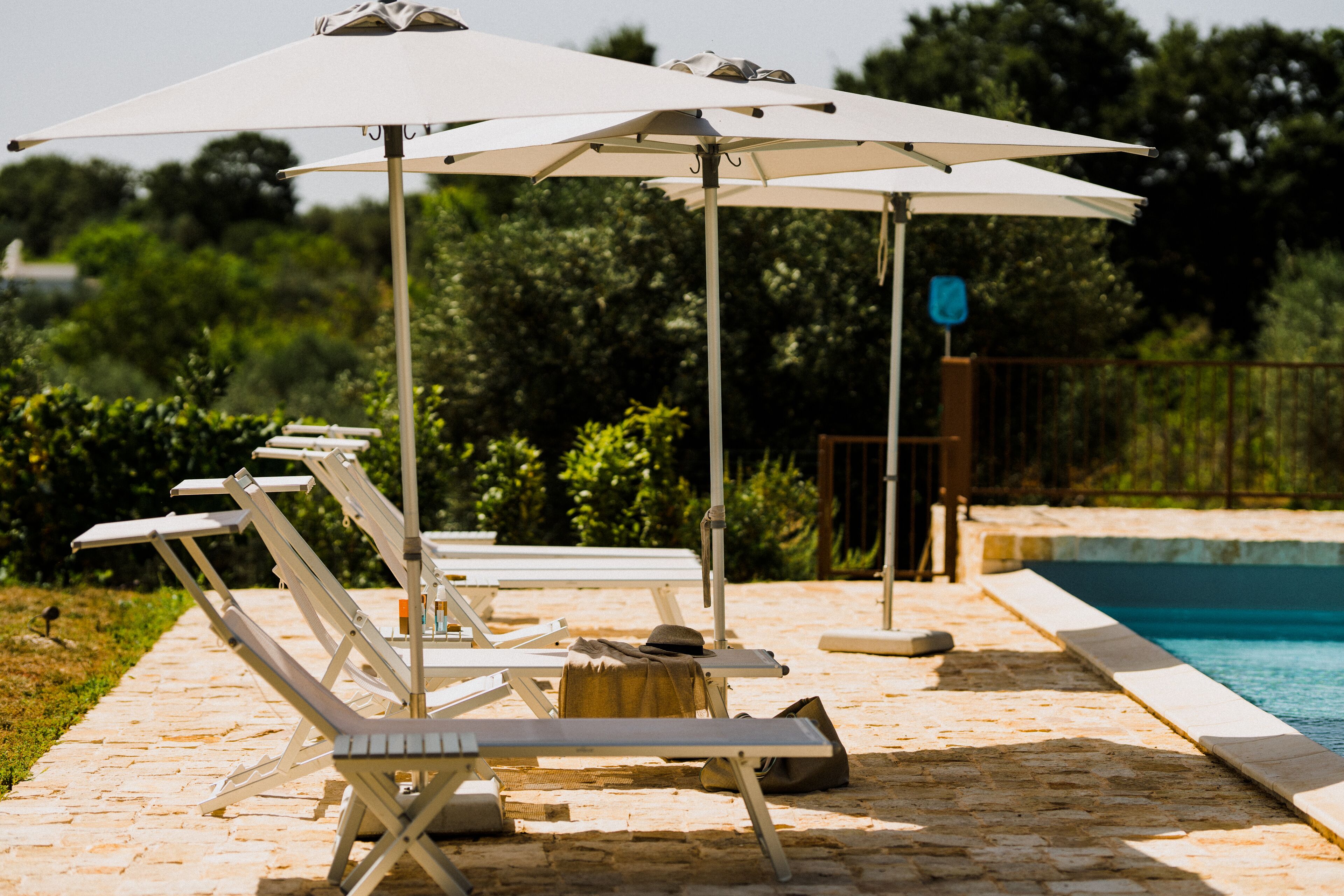 Un área junto a la piscina con sillones de descanso y sombrillas, un camino de piedra y una piscina.