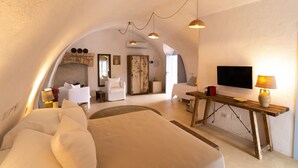 Una habitación acogedora y luminosa con una cama grande, una mesa de madera, un televisor y una zona de estar con una silla y un sofá.