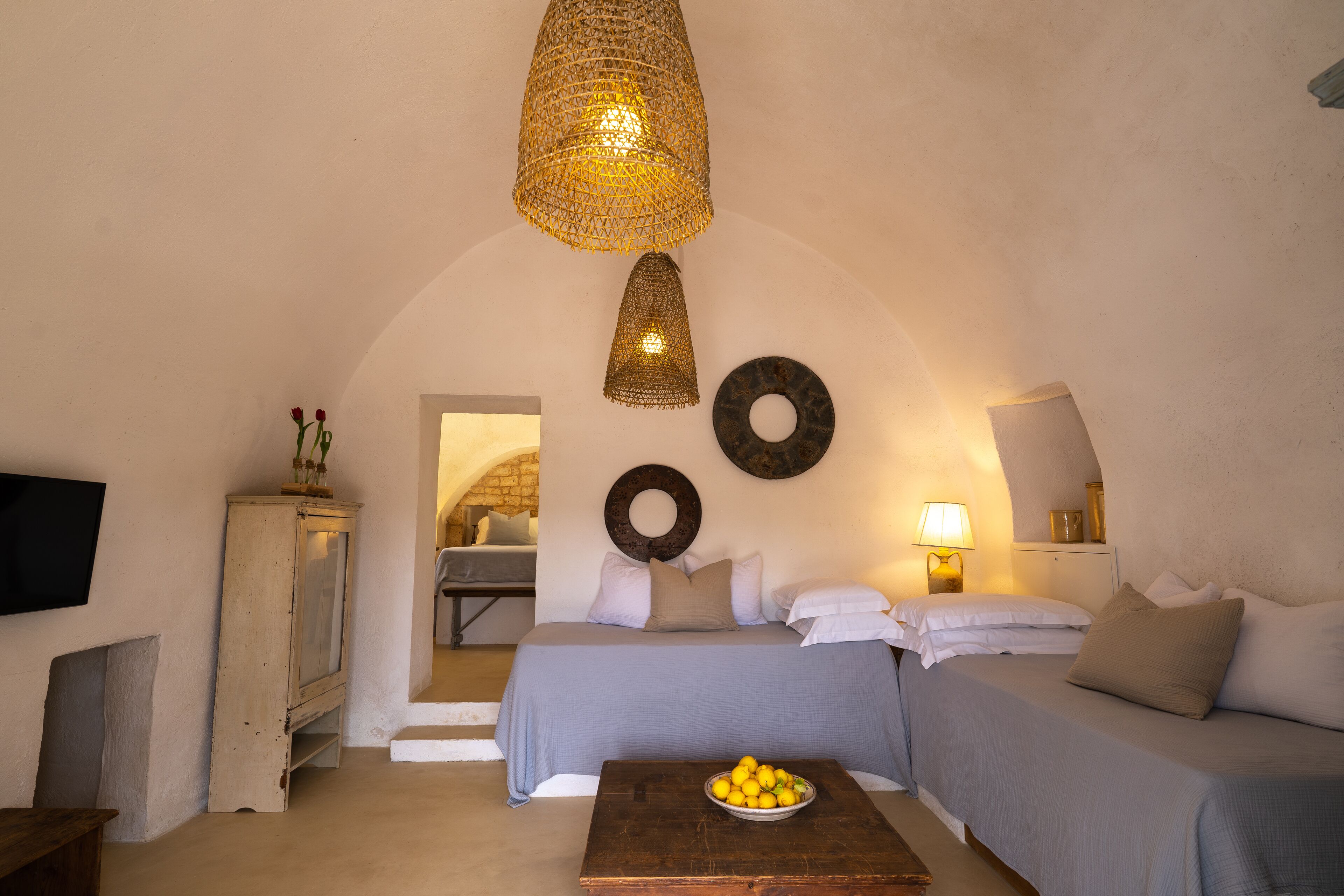 A cozy bedroom with a bed, a wooden table with a bowl of fruit, and a hanging light fixture.