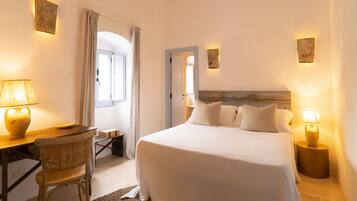 Una habitación de hotel con una cama grande, un escritorio con una lámpara, una silla y una mesita.
