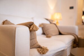 A white sofa with beige cushions and tassels, a lamp in the background, and a small table to the right. - Masseria Soluco (Monopoli)