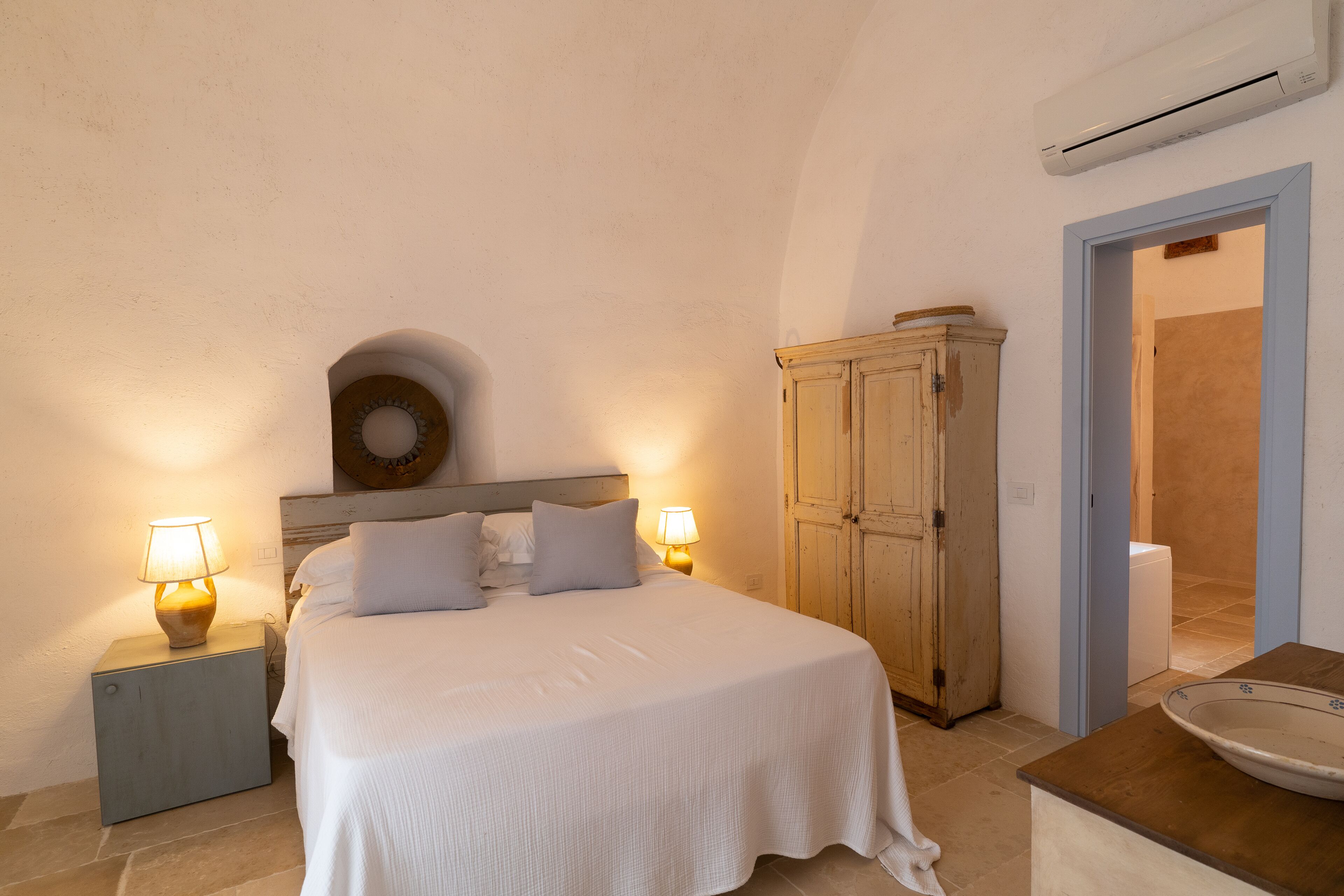 A bedroom with a bed, nightstands, a wardrobe, and an air conditioning unit.