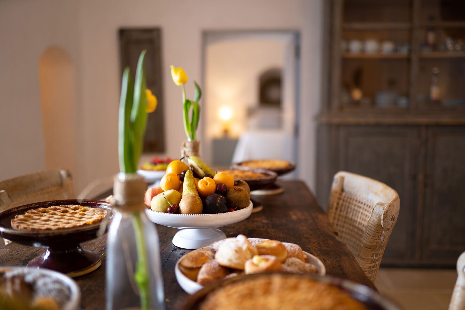 A dining table with various dishes, including a fruit arrangement, bread, and a pie.