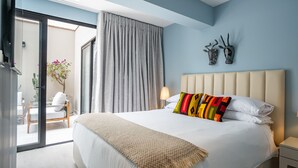 A bedroom with a bed, a nightstand, a lamp, and a view through a glass door to an outdoor seating area.