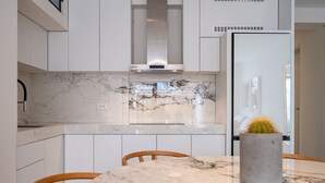 A modern kitchen with white cabinets, a marble countertop, and a built-in stove.