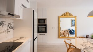 A modern kitchen with built-in appliances, a marble countertop, and a dining area with a mirror and chairs.