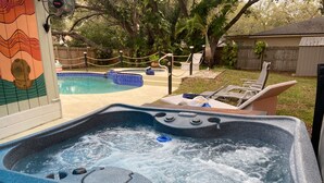 A hot tub with a control panel, surrounded by a wooden deck and a pool. - Pirate’s Cove (Tarpon Springs)