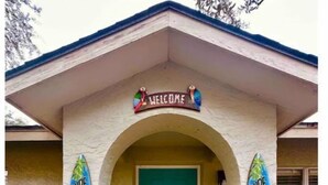 A building with a turquoise door, a 'Welcome' sign above, and 'Surf Shack' signs on either side. - Pirate’s Cove (Tarpon Springs)