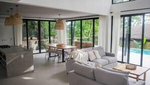 Ein modernes Wohnzimmer mit einer Couch, einem Esstisch und Stühlen, großen Fenstern und Blick auf Grünflächen.