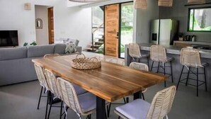 Ein stilvolles Wohnzimmer mit Esstisch aus Holz, Korbstühlen, einem grauen Sofa und einer Küchenzeile mit Barhocker.