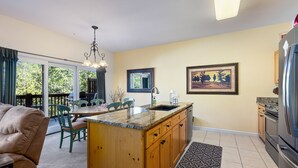 A kitchen with wooden cabinets, a granite countertop, and a built-in sink. There is a dining area with a table and chairs, and a large window providing a view of the outdoors.