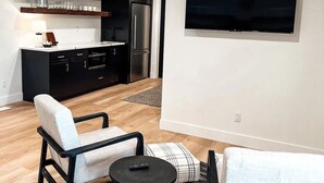A modern living room with a flat-screen TV mounted on the wall, a sofa, a chair, and a small coffee table.