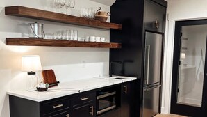 A modern kitchen with dark cabinetry, wooden shelves, and a stainless steel refrigerator.