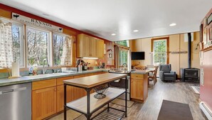 A modern kitchen with wooden cabinets, a large island, and a dining area with a fireplace. - Stratton; 6 min. King beds. Pool Table. Wood Stove. Dog friendly (Jamaica)