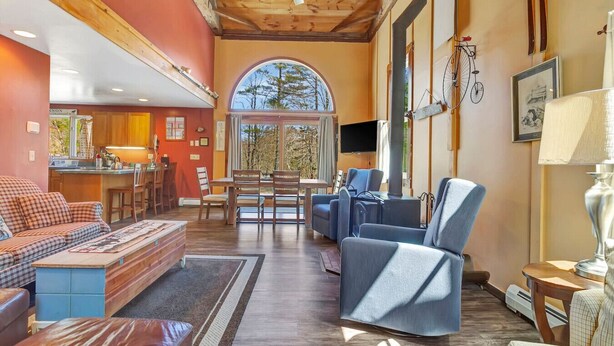 A cozy living room with a sofa, chairs, a dining table, and a large window. - Stratton; 6 min. King beds. Pool Table. Wood Stove. Dog friendly (Jamaica)