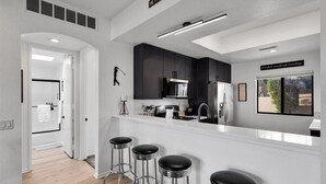A modern kitchen with dark cabinets, a white countertop, and three bar stools.
