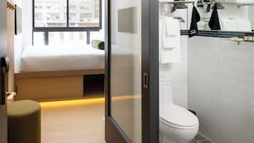 Quarto de hotel moderno com uma cama, um toalete e zona de chuveiro.