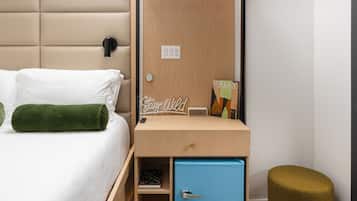 Un dormitorio moderno con cama, mesita de noche de madera, unidad de almacenamiento azul, cojín verde, taburete pequeño y tragaluz.