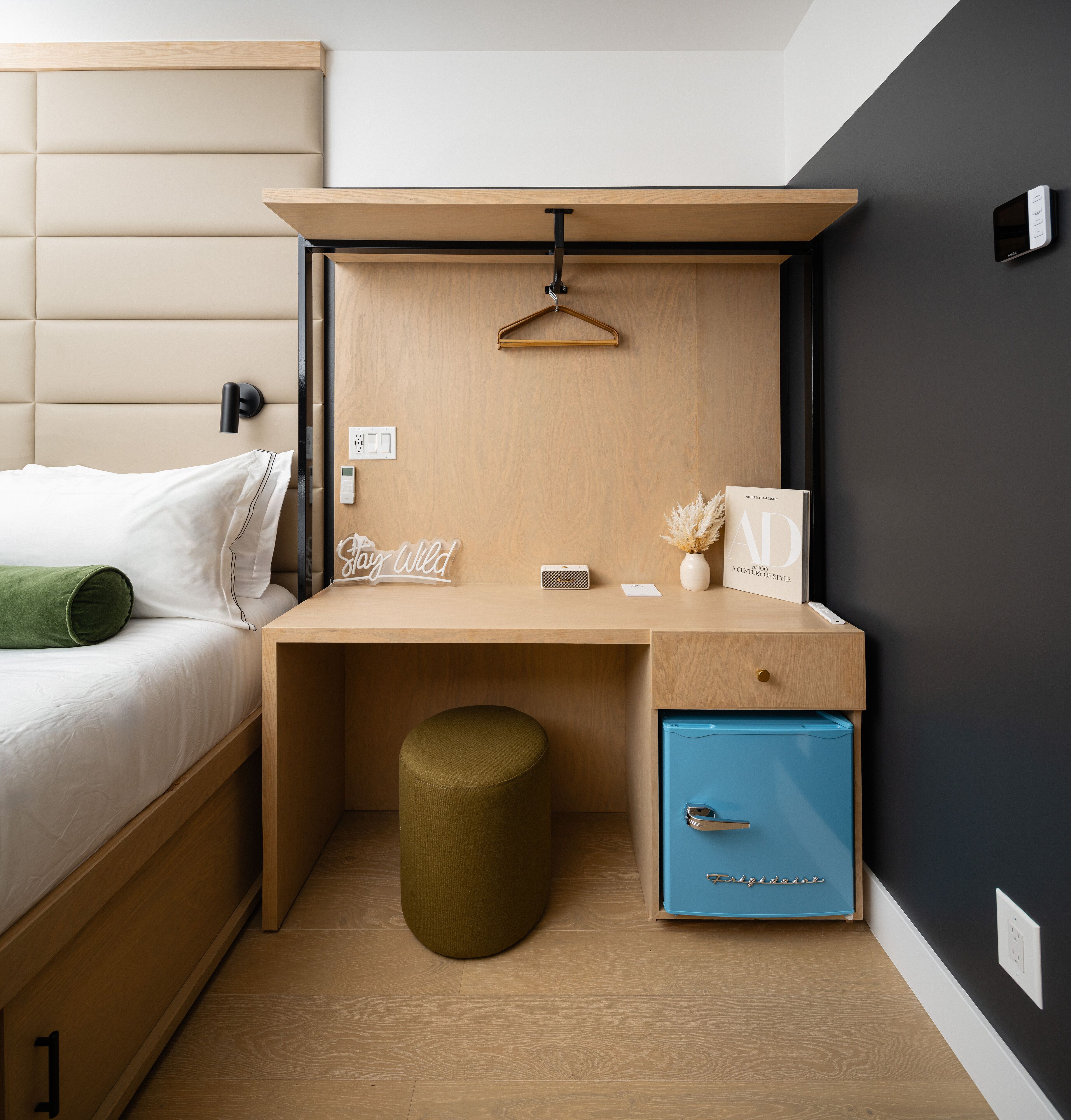 Quarto moderno com cama, mesa de cabeceira, escrivaninha e um pequeno armário azul.